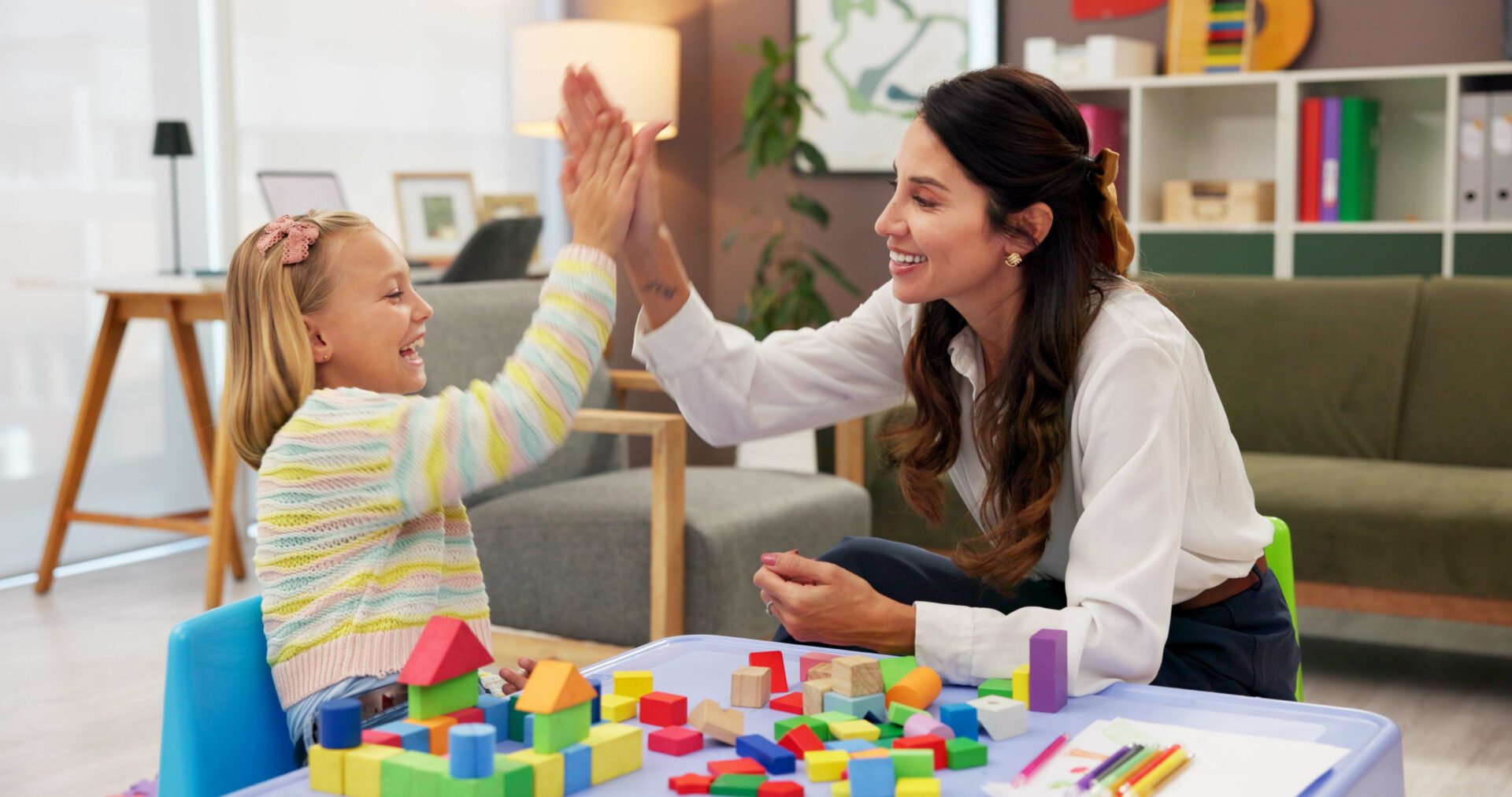 An image of a therapist and a child giving a high five while playing with building blocks.